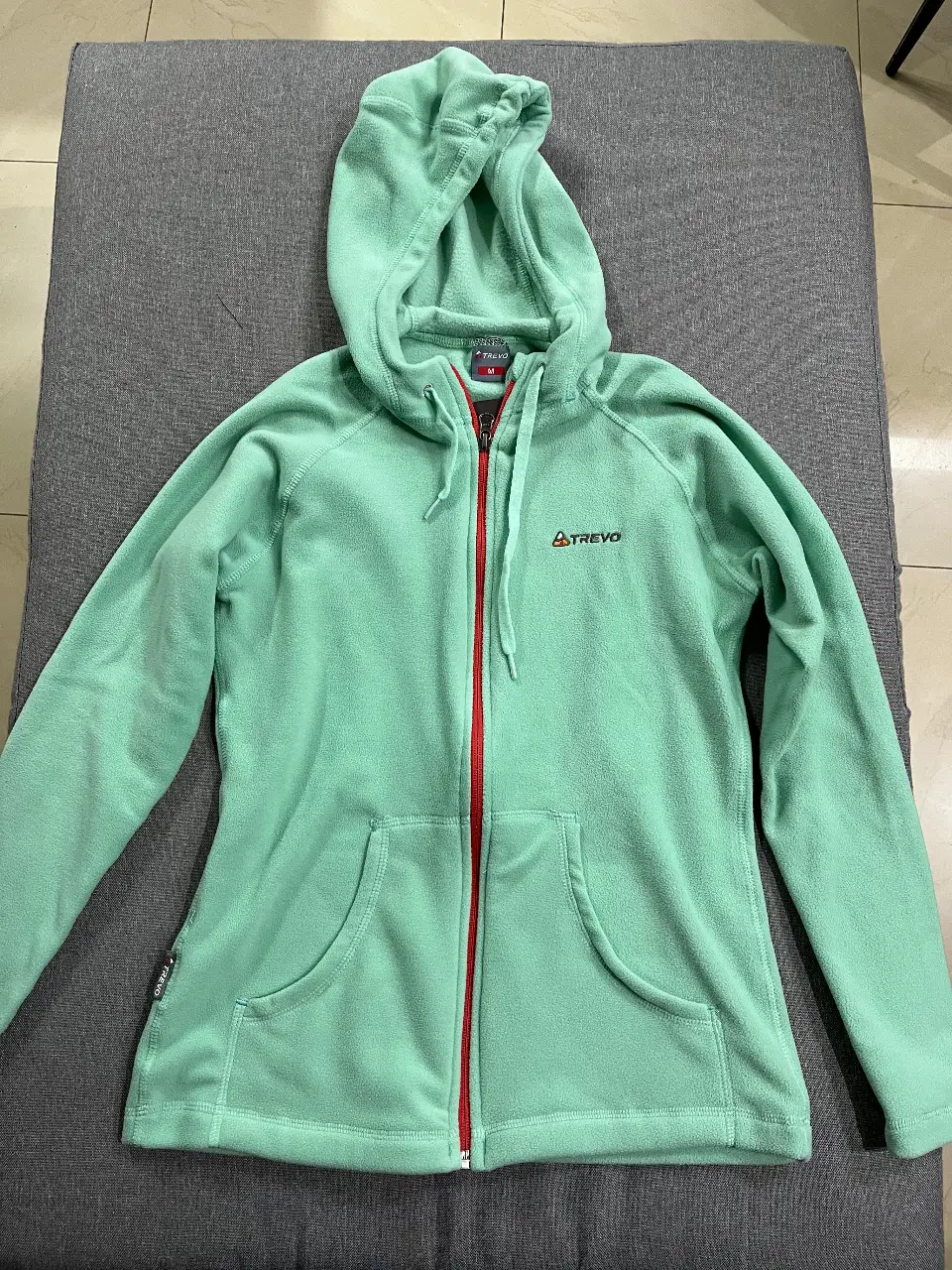 Buzo con cierre y capucha de la marca Trevo, color verde agua. Ideal para actividades al aire libre o para usar en el día a día. Confeccionado en polar, ofrece abrigo y comodidad. Talle M.