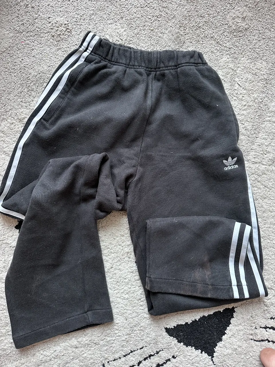 Pantalón de jogging Adidas negro con las clásicas tres tiras blancas en los laterales. Ideal para un look deportivo y cómodo. TIENE MANCHA DE LAVANDINA ABAJO