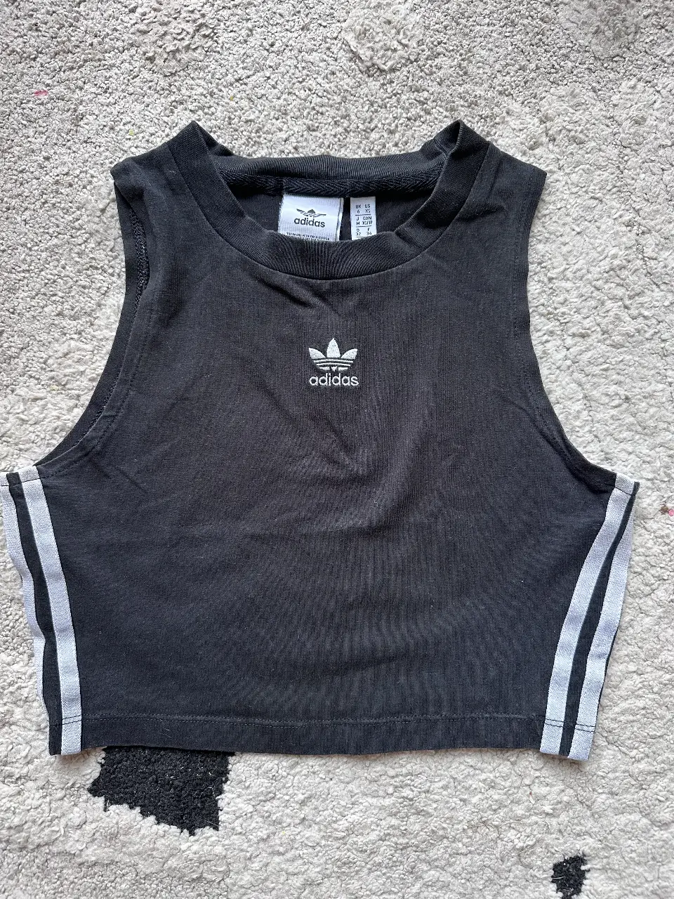 Top deportivo negro de Adidas, con el logo icónico de la marca. Ideal para entrenamientos o un look casual y moderno. Confeccionado en algodón y elastano para mayor comodidad y ajuste.