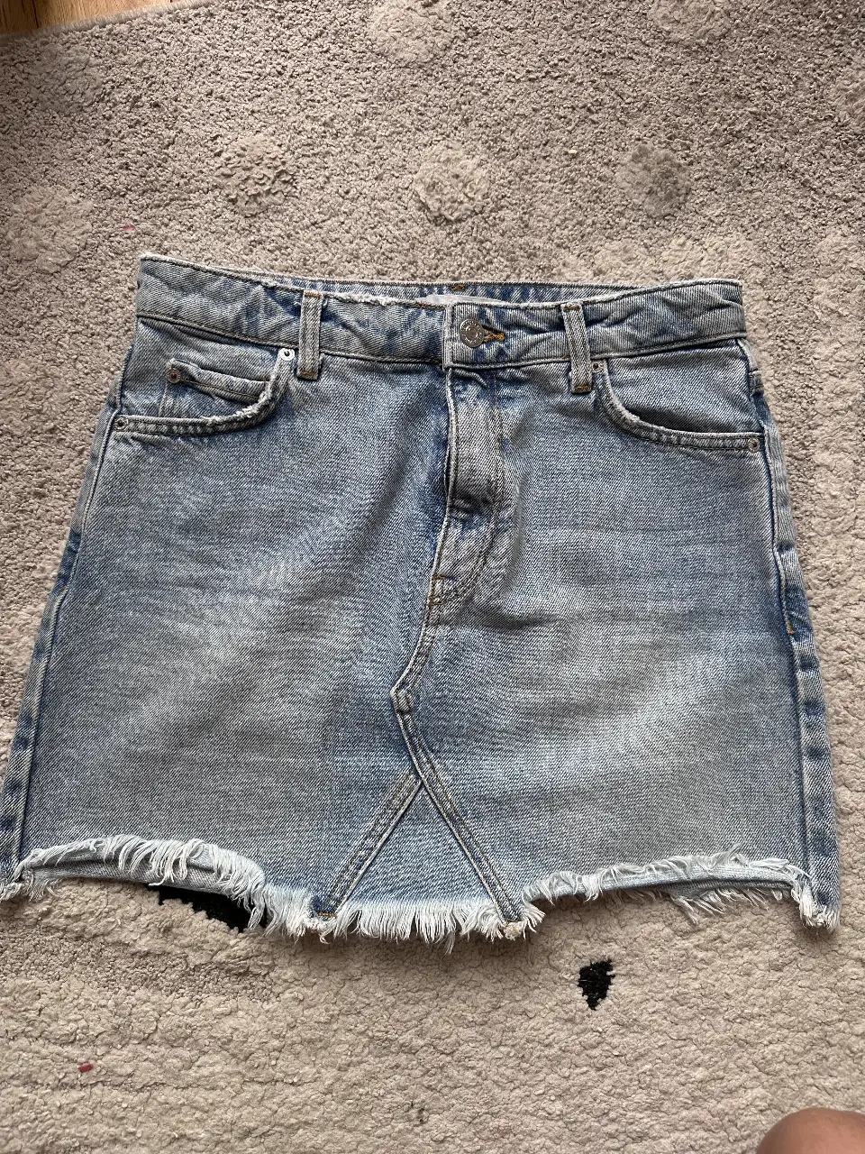 Minifalda de jean azul claro con detalles desflecados en el borde inferior. Ideal para un look casual y moderno.