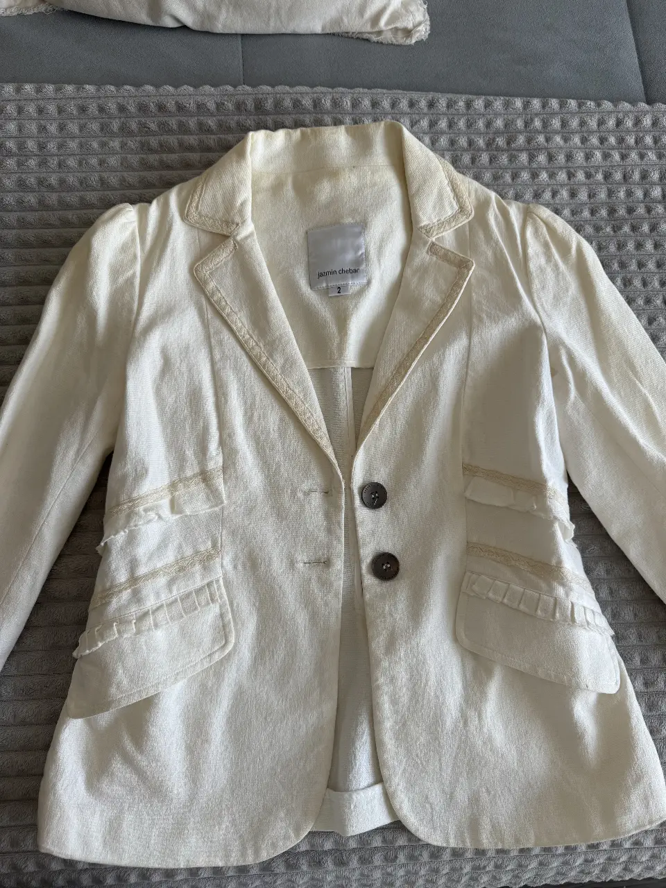 Blazer blanco de la marca Jazmin Chebar, con detalles de encaje en solapas y bolsillos. Talle 2.