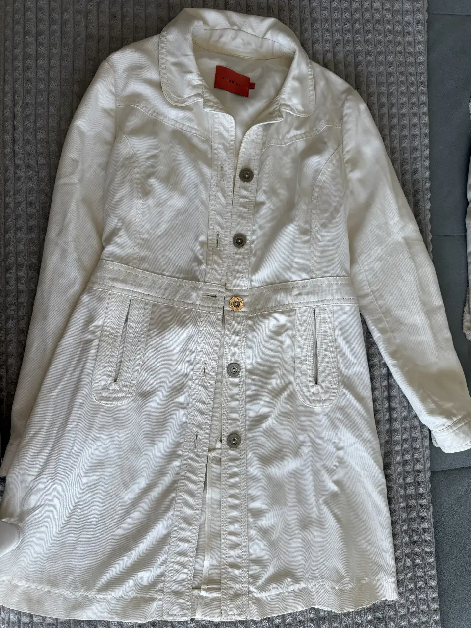 Campera de jean blanca de la marca Vitamina, con botones y cinturón. Ideal para un look casual y elegante.