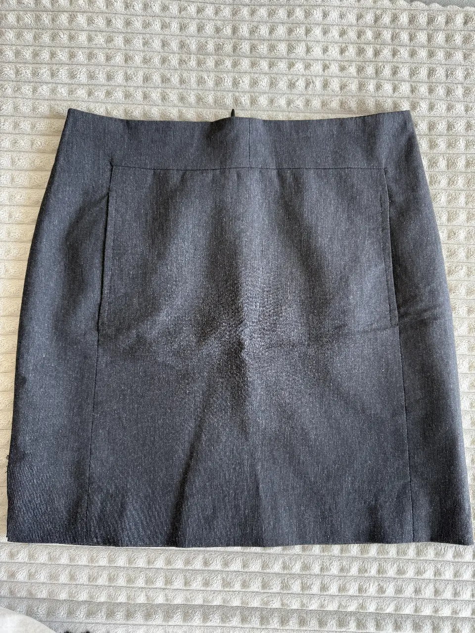 Pollera sastrera gris, con un diseño clásico y elegante. Ideal para un look formal o de trabajo. Cuenta con un bolsillo lateral y cierre trasero.