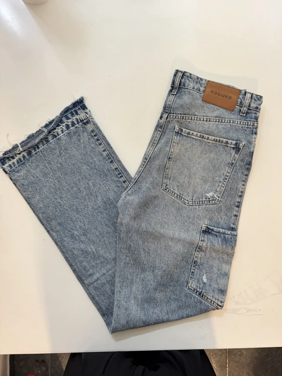 Jeans de tiro alto con roturas y detalles desgastados en los bolsillos y botamangas. Poseen un bolsillo cargo en el lateral derecho y un diseño de lavado claro.