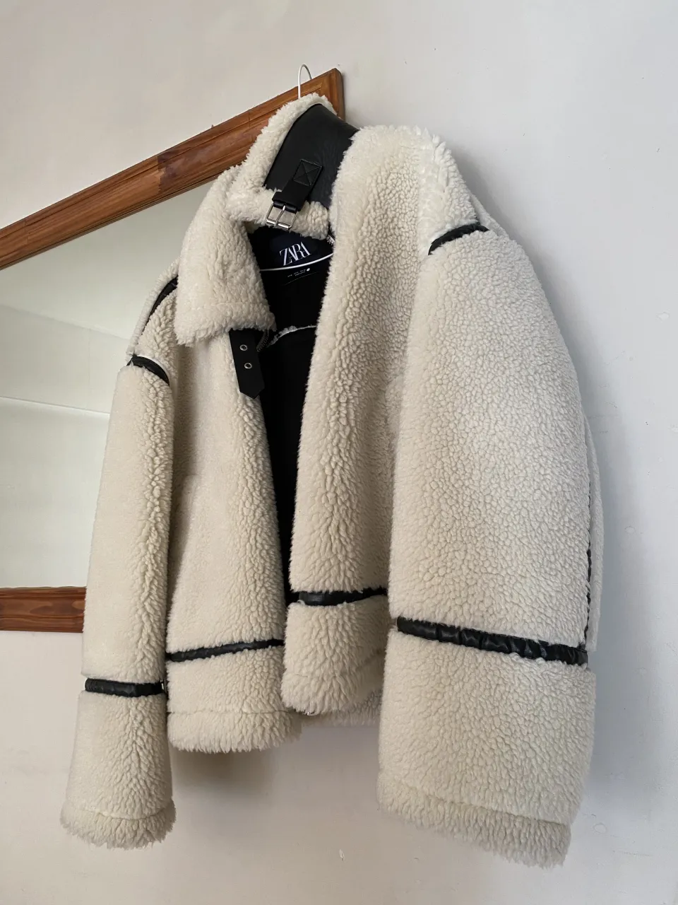 Campera  Zara de abrigo color blanco roto con detalles y ribetes en negro. Tiene cuello con hebilla y puños ajustables con hebilla.