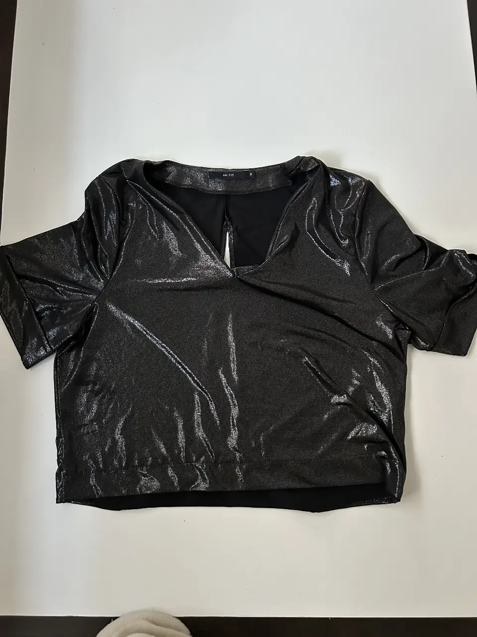 Crop top negro brillante con escote en V y detalle de abertura en la espalda. Ideal para fiestas y eventos. Talle M