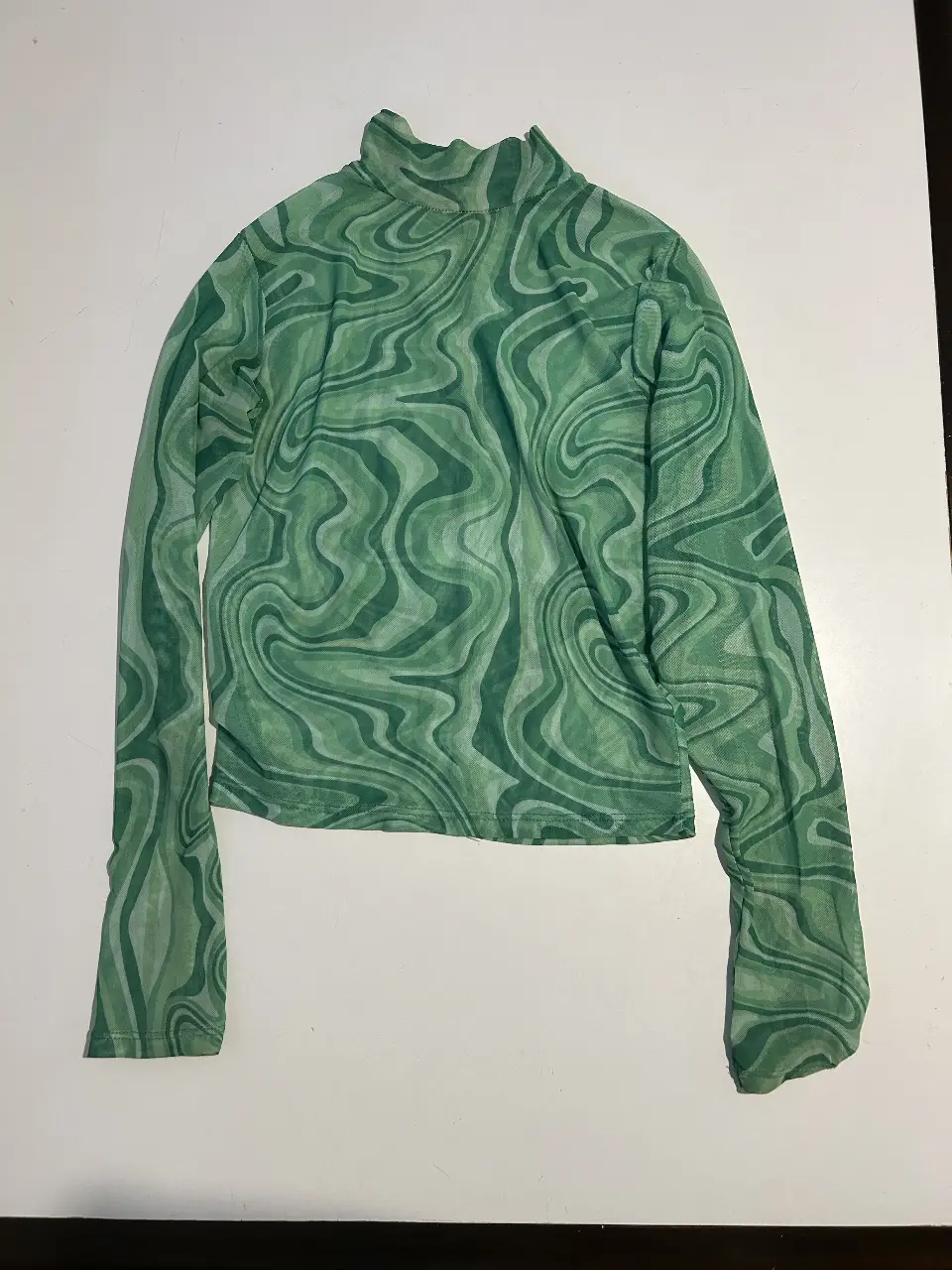 Remera manga larga con cuello alto y estampado. Tela traslucida. Ideal para un look moderno y audaz.