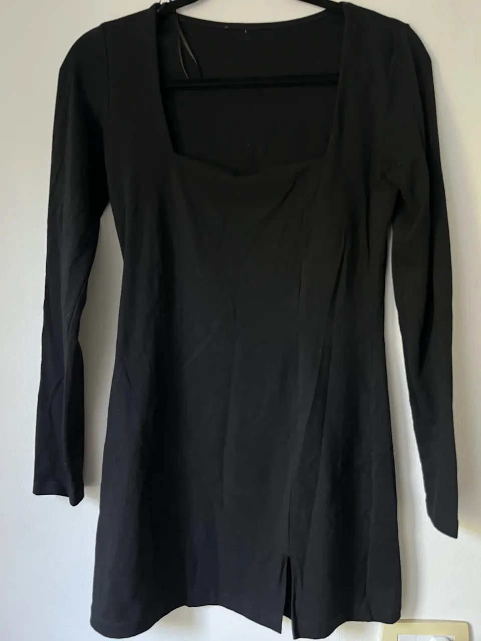 Vestido negro de manga larga con escote cuadrado y tajos laterales en el ruedo.