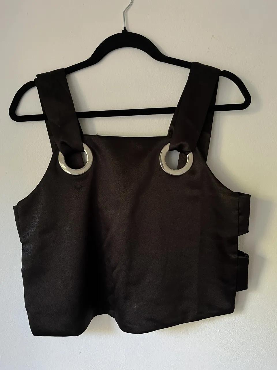 Top negro con tiras anchas y detalles de argollas metálicas en la parte delantera. Posee cortes laterales con tiras. 
es un S/m