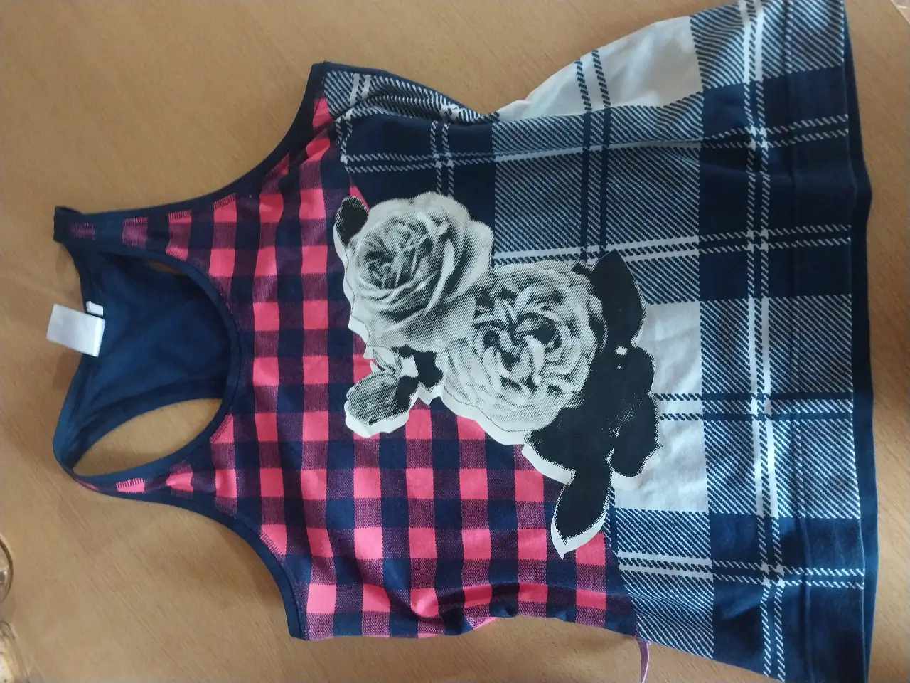 Musculosa deportiva para mujer, con estampado de rosas en blanco y negro sobre un fondo a cuadros rosa y azul marino. Diseño moderno y cómodo para actividades físicas.