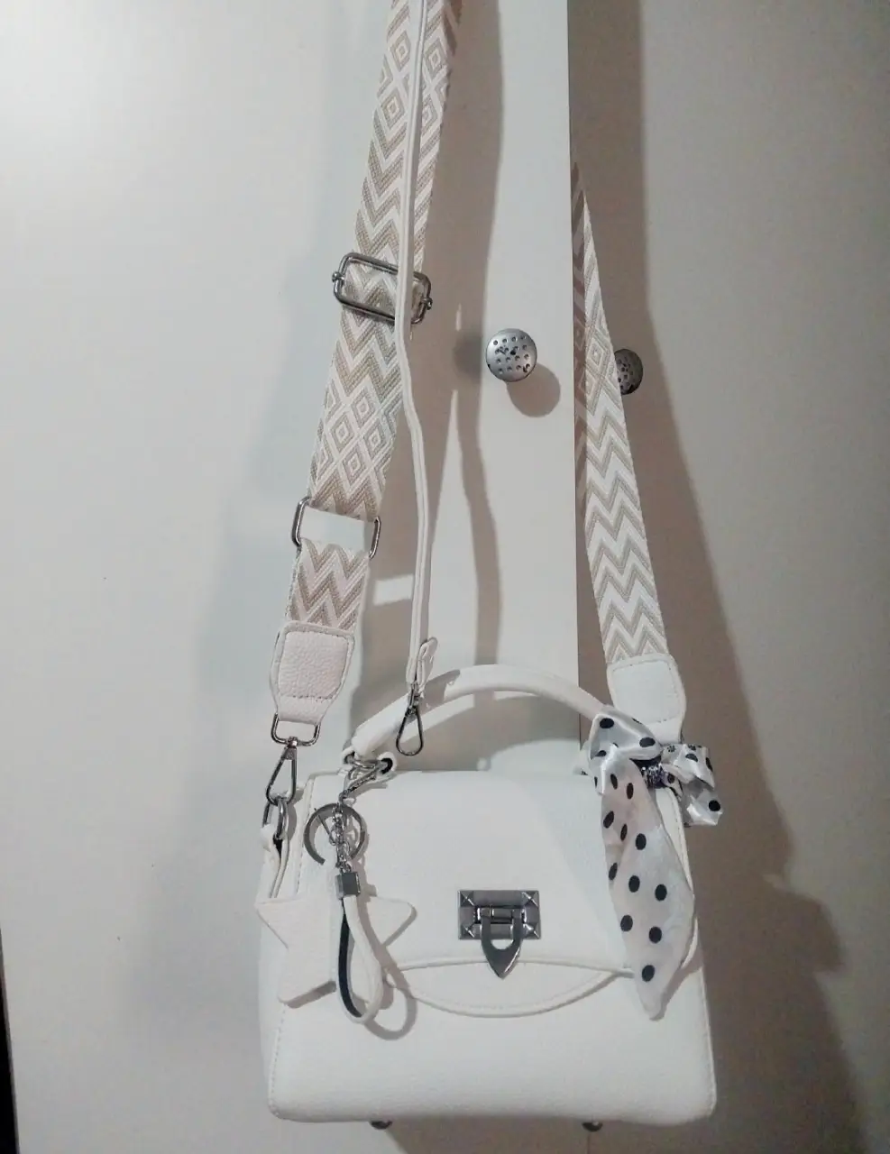 Cartera blanca con correa ajustable y detalle de pañuelo con lunares. Incluye llavero con dije de estrella.