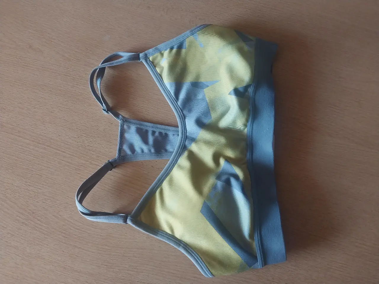 Top deportivo para mujer, con diseño geométrico en tonos amarillo y gris. Ideal para actividades de bajo impacto. Confeccionado con materiales transpirables y de secado rápido.