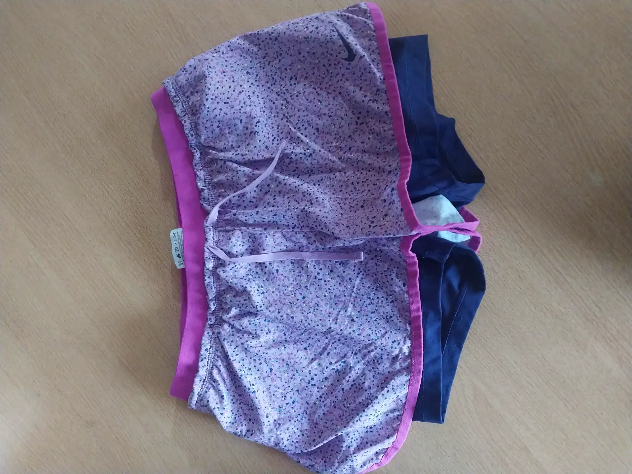 Short deportivo Nike Dri-Fit para mujer, con estampado floral en tonos lilas y rosa, con detalles en azul marino y cintura rosa. Ideal para running y entrenamientos.