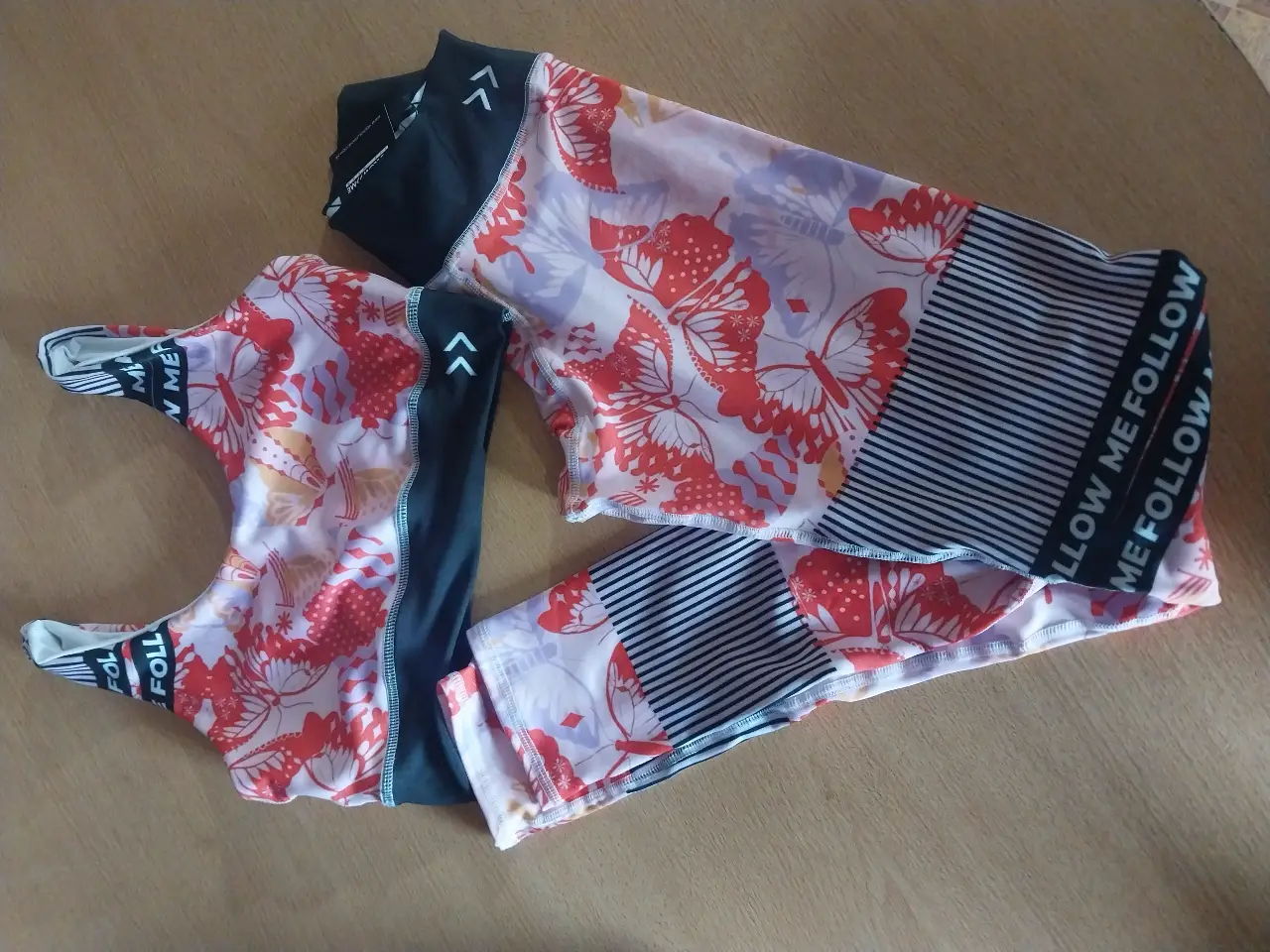 Conjunto deportivo de calzas y top con estampado de mariposas. Las calzas tienen detalles en negro y la frase "FOLLOW ME FOLLOW ME". Ideal para entrenar con estilo.