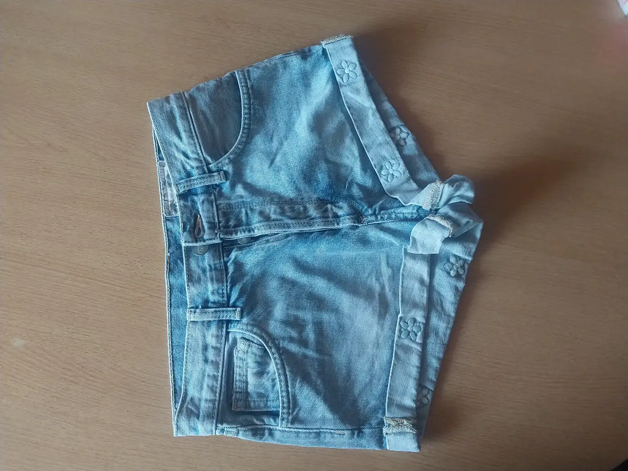 Short de jean azul claro, con detalles de flores en los bordes. Tiro medio, ideal para el verano. Perfecto para un look casual y fresco.