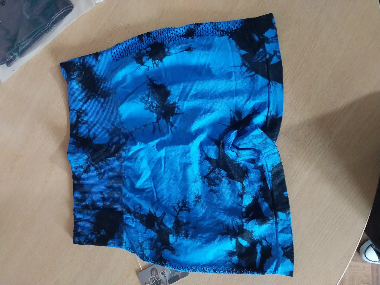 Top deportivo sin costuras, con diseño tie dye en tonos azul y negro. Ideal para entrenamientos de alto impacto, ofrece soporte y comodidad.