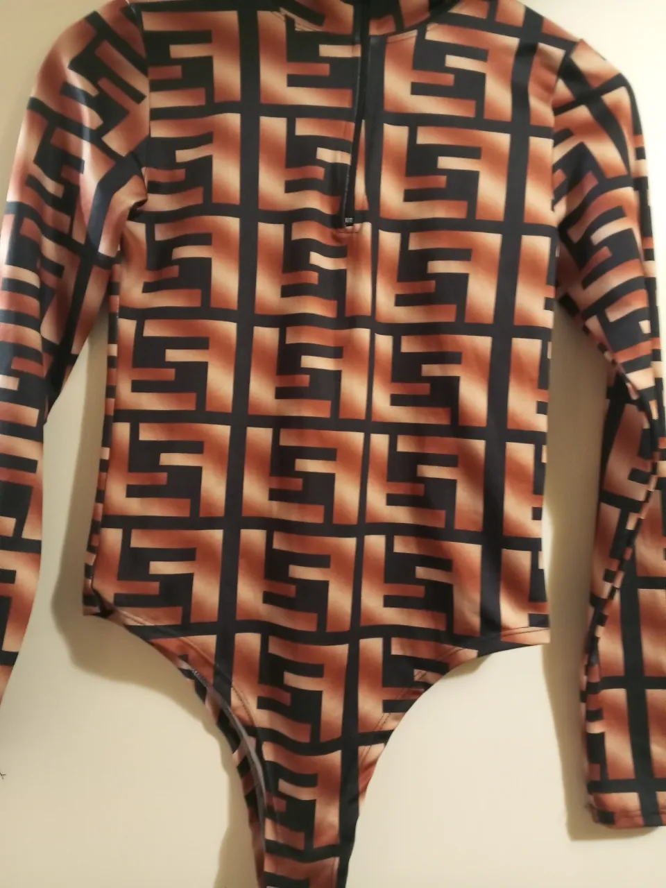 Body de mujer con estampado geométrico en tonos marrones y negros. Cuello alto y cierre frontal. Ideal para un look moderno y audaz.