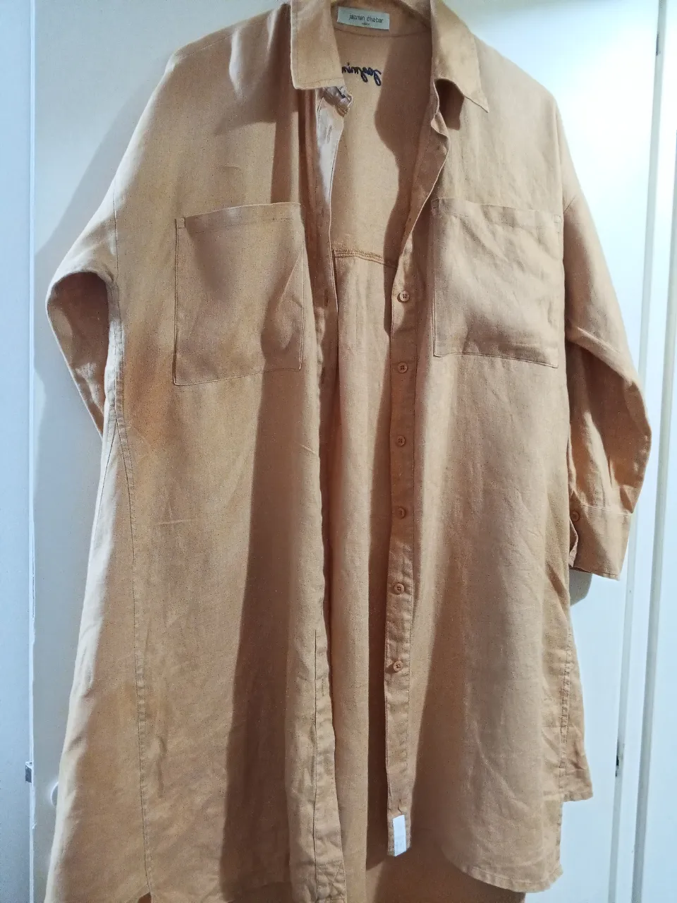 Camisa larga de lino color marrón claro, con dos bolsillos delanteros y botones. Ideal para un look casual y relajado.