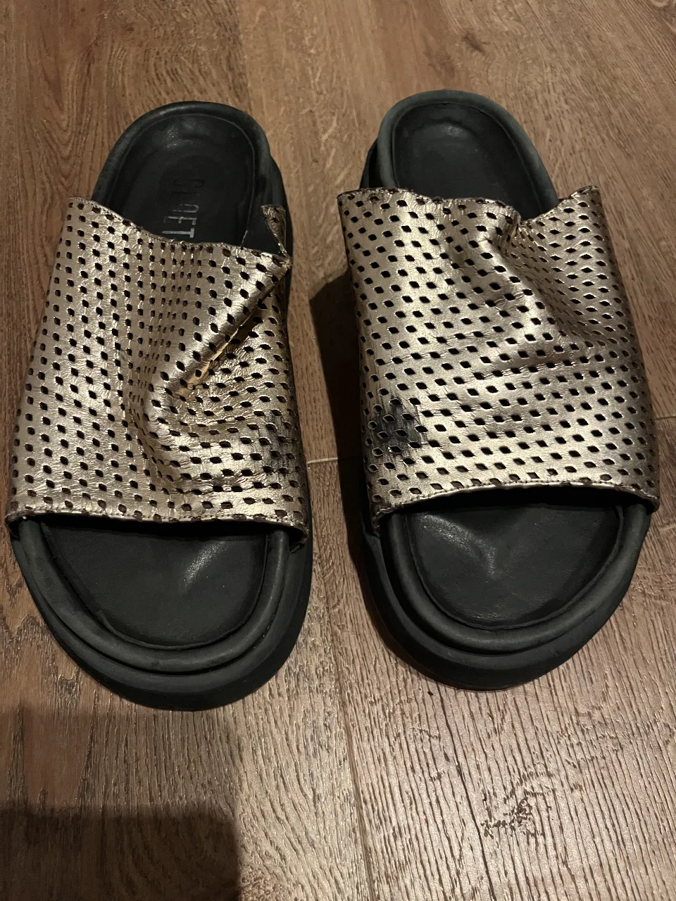 Sandalias tipo chinelas súper cómodas y cancheras. Tienen un diseño moderno con tiras perforadas en dorado metalizado y base negra. Ideales para el día a día, para estar fresca y con estilo.