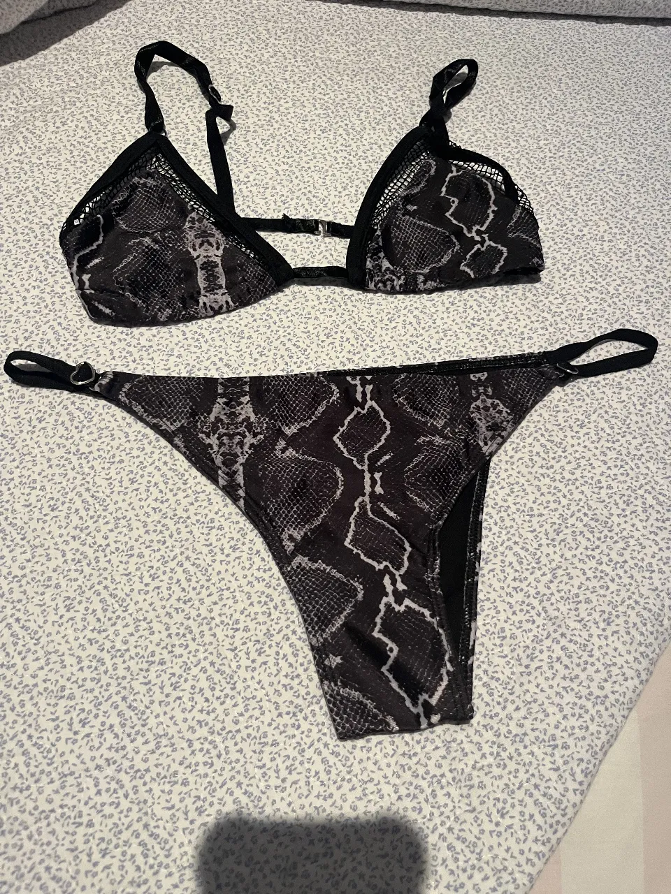 Conjunto de bikini estampado de serpiente en tonos negro y gris. El corpiño es triangular con detalles de red y tiras regulables. La bombacha es colaless con tiras laterales regulables.