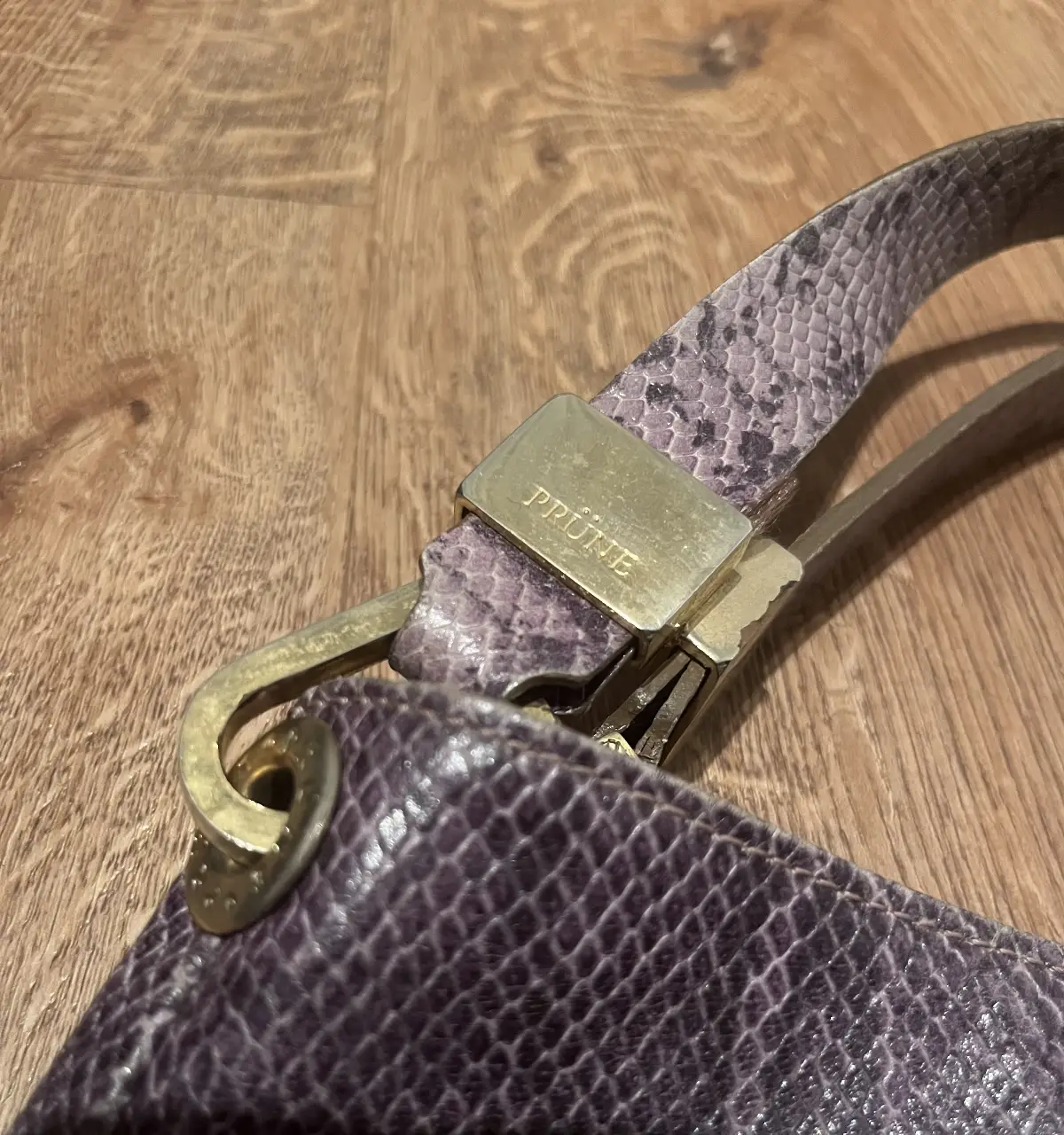 Cartera de hombro PRUNE, de cuero con diseño símil piel de serpiente en tonos violetas. Detalles dorados y correa ajustable.