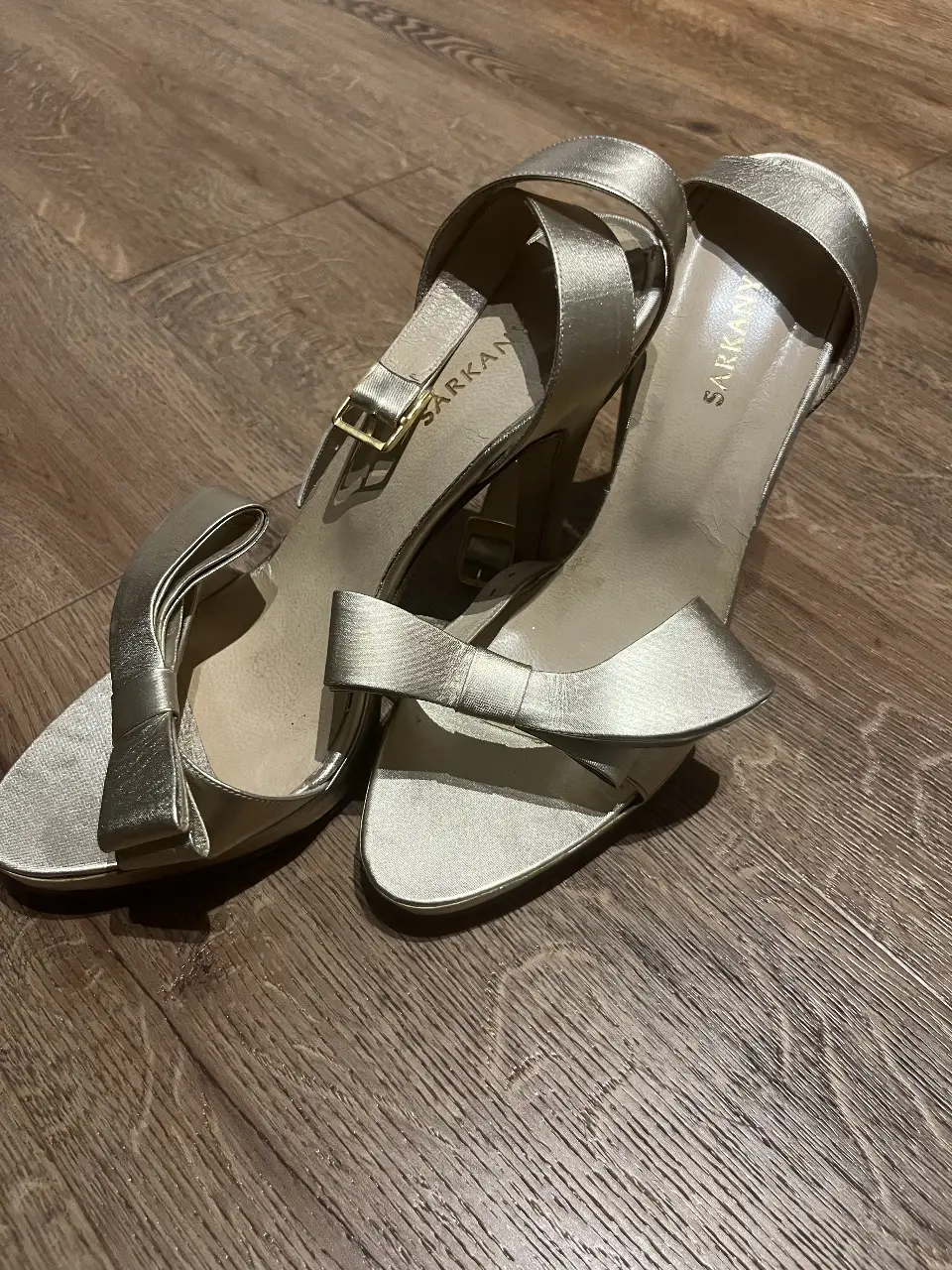 Sandalias doradas de tacón alto con detalles de moño en la parte delantera. Ideales para eventos formales y fiestas.