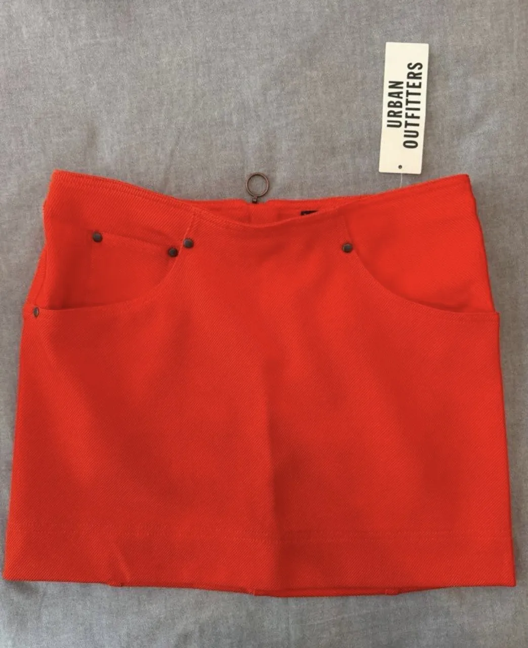 Pollera corta de color rojo vibrante. Tiene bolsillos delanteros y detalles metálicos en la cintura.