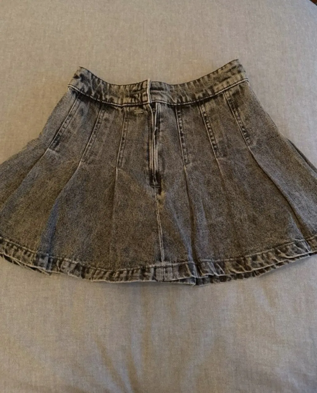 Pollera de jean gris con efecto desgastado. Tiene pliegues en la parte delantera y cierre.