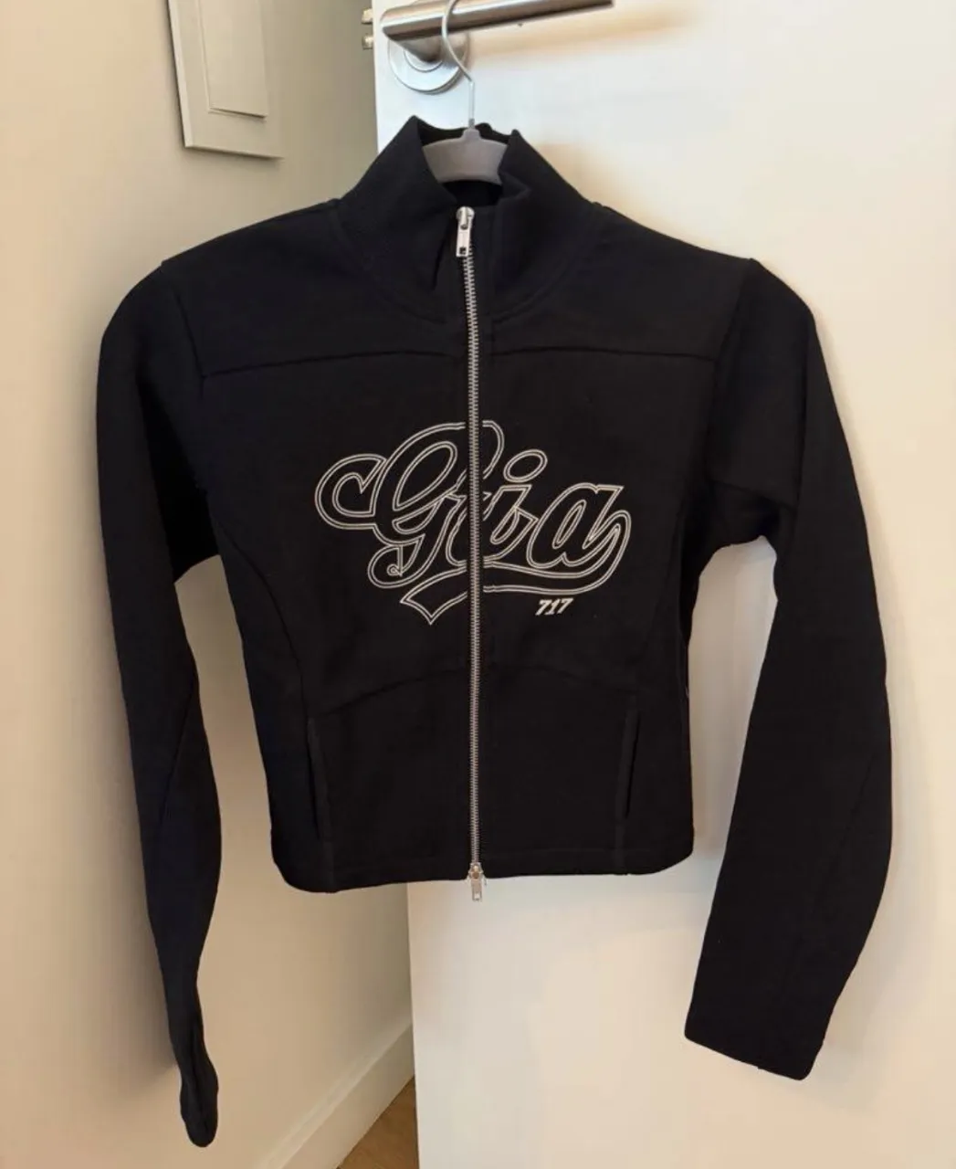 Campera negra con cierre central y logo blanco bordado en el frente.