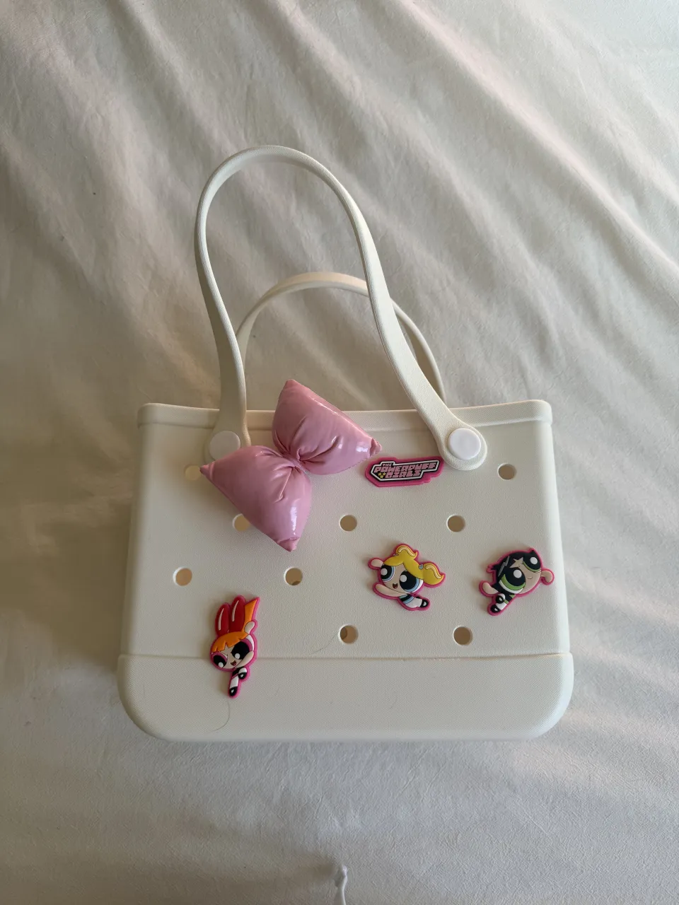 ¡Cartera súper linda y original! Perfecta para darle un toque divertido a tu look. Viene con charms de las Powerpuff Girls y un moño rosa, ¡ideal para las fans! Es blanca y muy práctica.