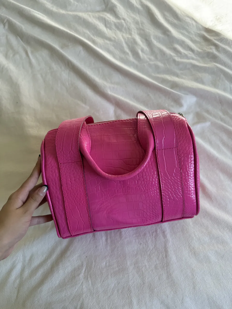 Bolso rosa fucsia con textura de cocodrilo. Tiene dos asas cortas y cierre metálico. Ideal para darle un toque de color a cualquier outfit.