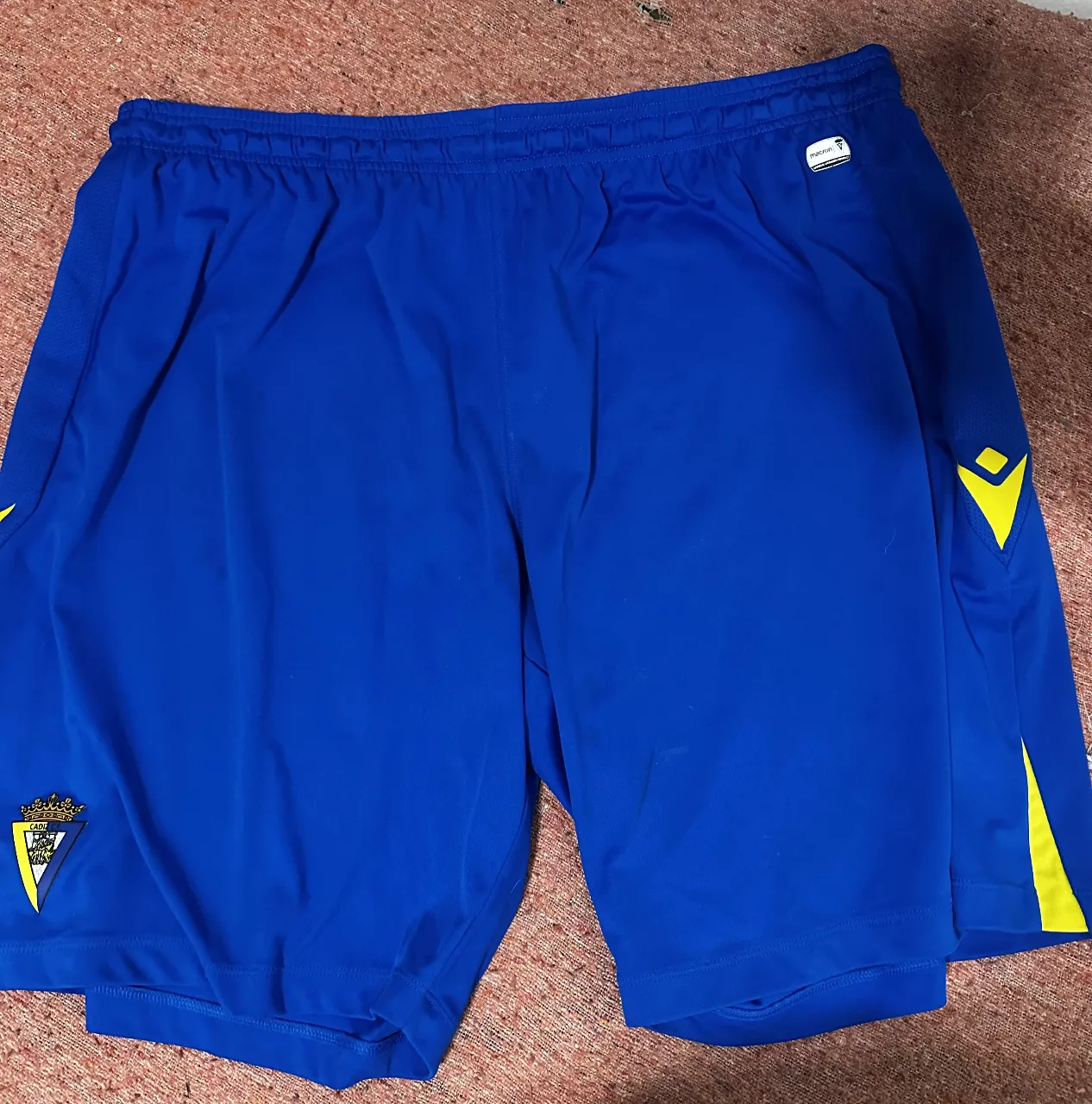 Short deportivo original de club Cádiz de España azul con detalles amarillos, ideal para entrenamientos y actividades físicas. Con logo de la marca y talle 4XL.