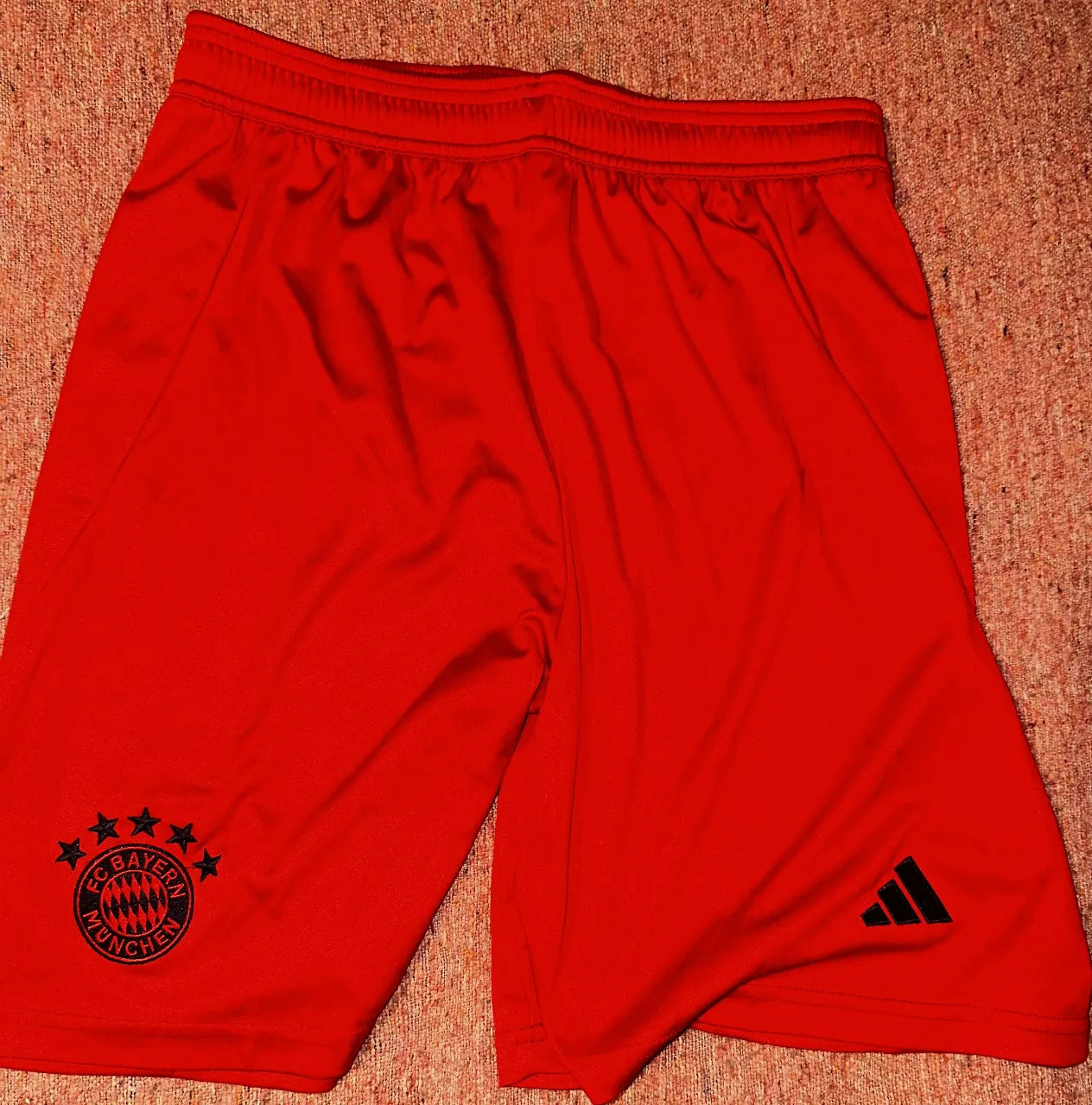 Short deportivo de hombre, color rojo, con el escudo del Bayern Munich y el logo de Adidas en negro. Confeccionado con tecnología Aeroready para mayor comodidad y rendimiento.