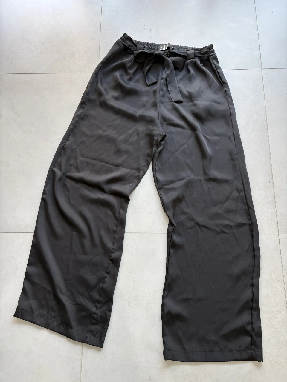 Pantalón negro con lazo en la cintura, es fino y de tela un poco brillosa. ideal para salidas de noche más arregladas. si bien la cintura tiene elástico atras, no se estira tanto entonces puede que no pase por la cadera. 
cintura 40cm / cadera 60cm 