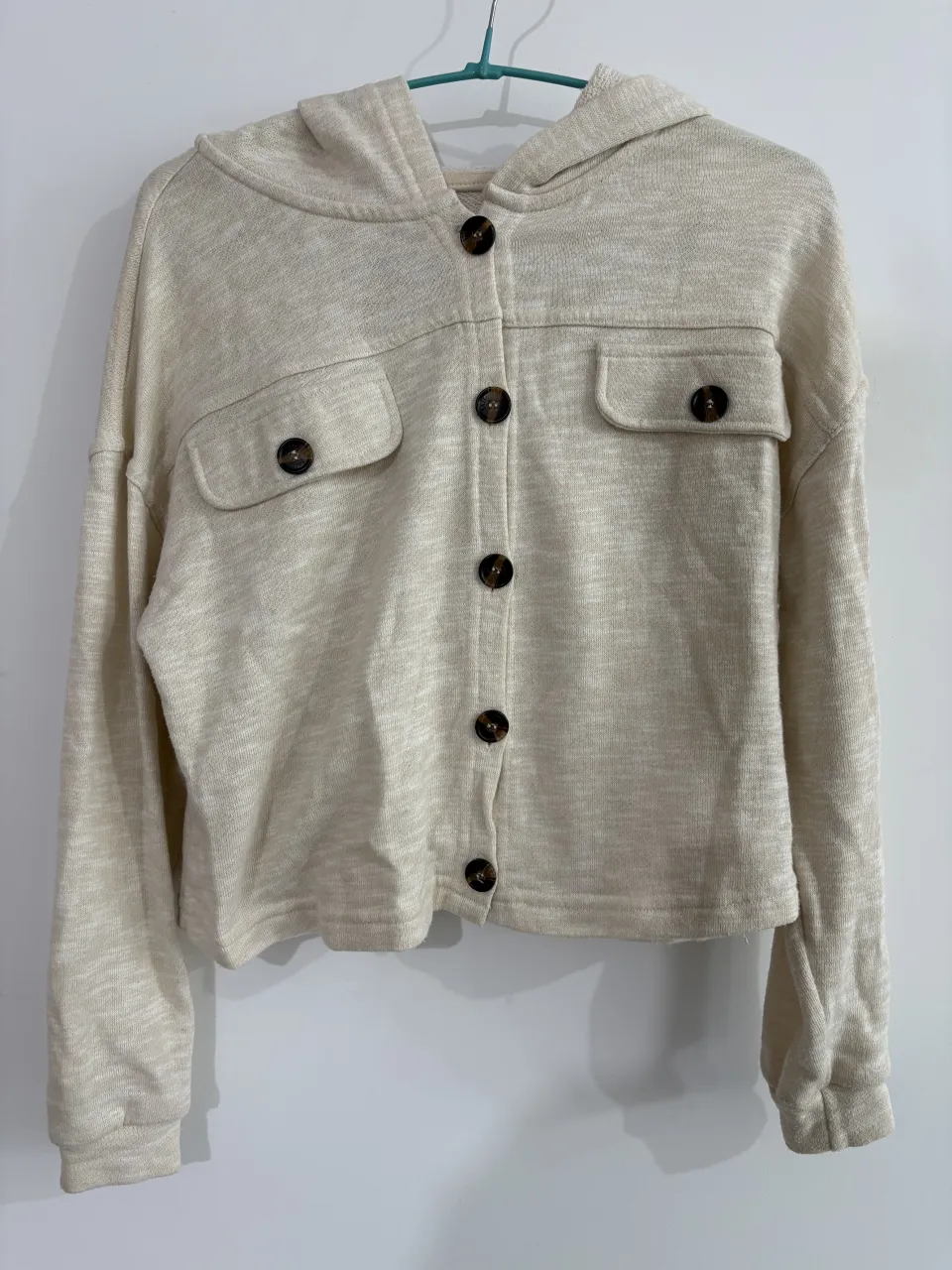 campera crop con capucha, botones al frente y dos bolsillos en el pecho. Tejido de punto color crudo.