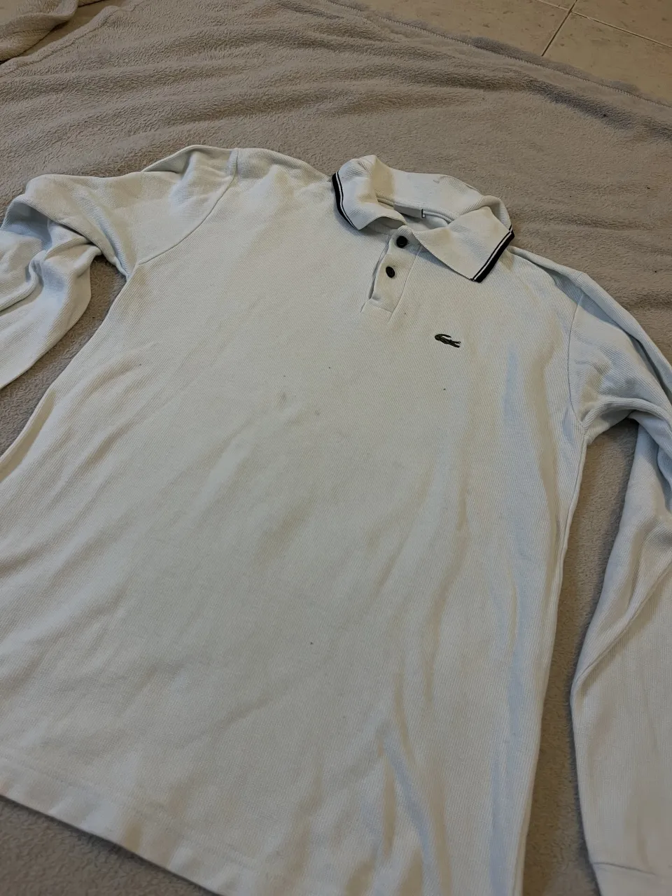 Remera polo manga larga blanca con cuello y puños a rayas negras. Posee dos botones en la parte superior y un pequeño logo bordado en el pecho.