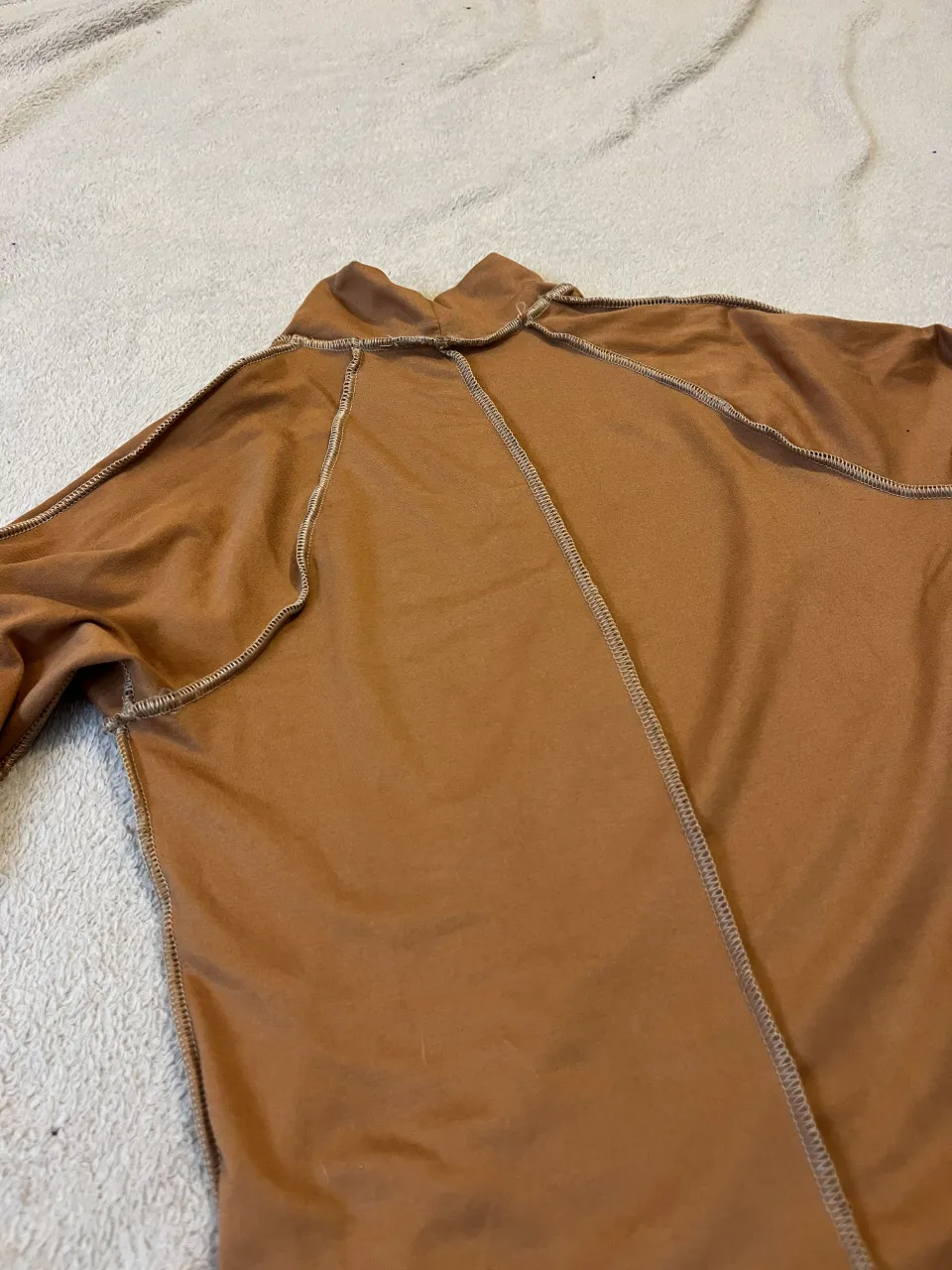 Remera manga larga de cuello alto con costuras expuestas en color marrón. El cuello es tipo polera.