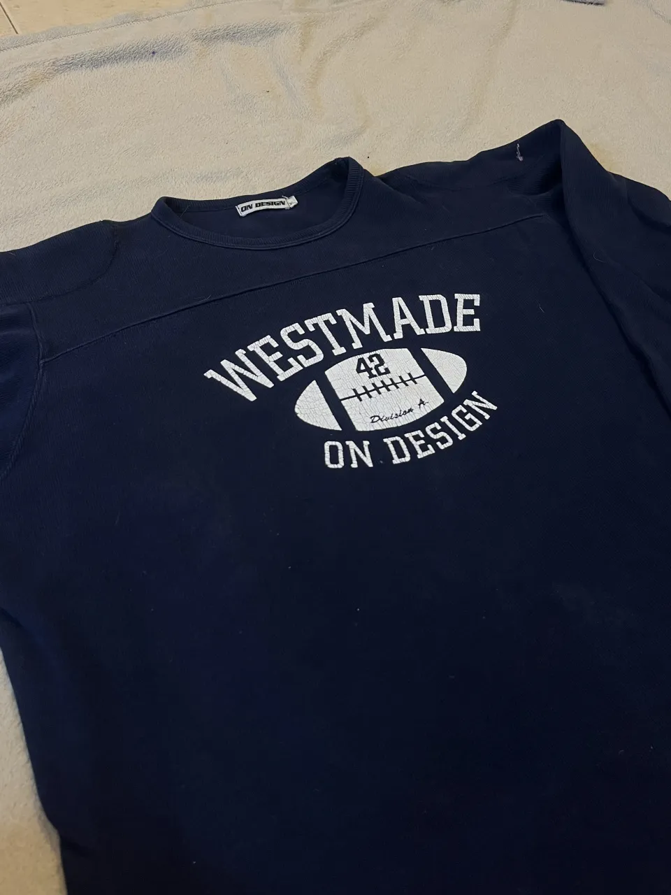 Remera vintage azul marino con estampa de pelota de fútbol americano y texto "WESTMADE ON DESIGN".