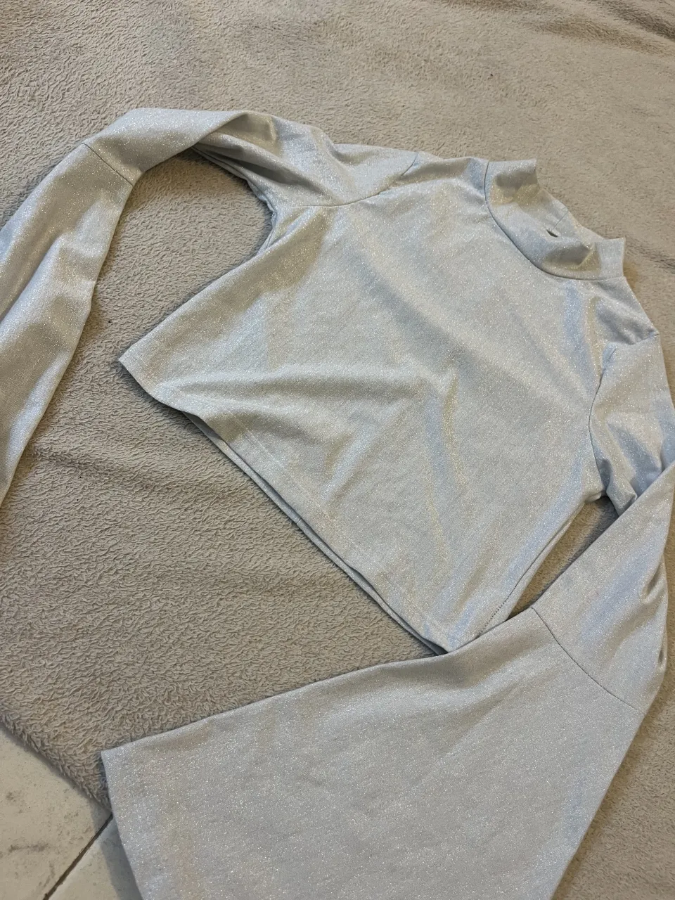 Remera plateada con brillos y cuello alto. Mangas largas acampanadas. no tiene talle pero es aprox un M esta con MUY POCO USO