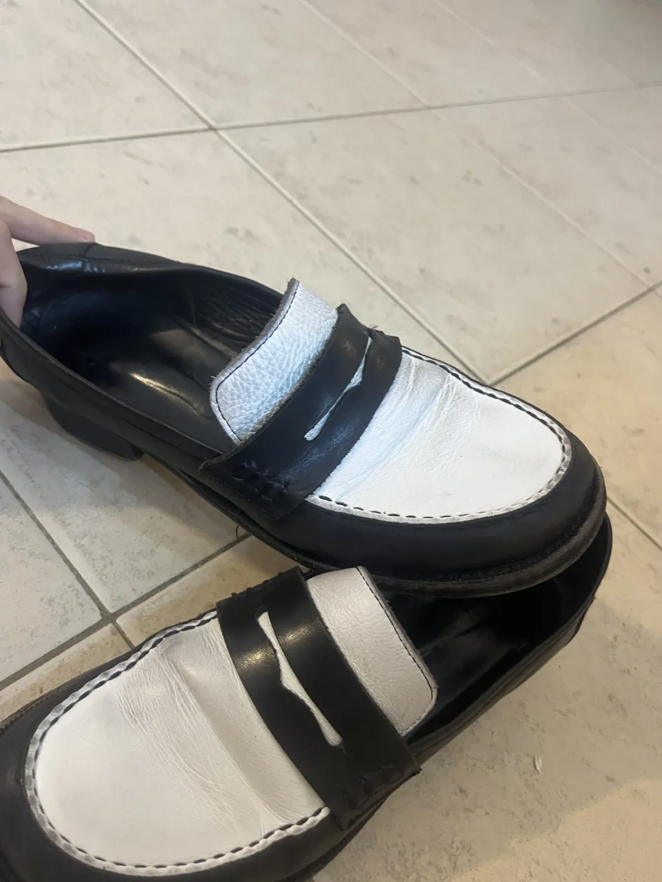 Zapatos mocasines de cuero, estilo clásico con detalle de tira y costuras a la vista. Diseño bicolor en blanco y negro, perfectos para un look casual o elegante.