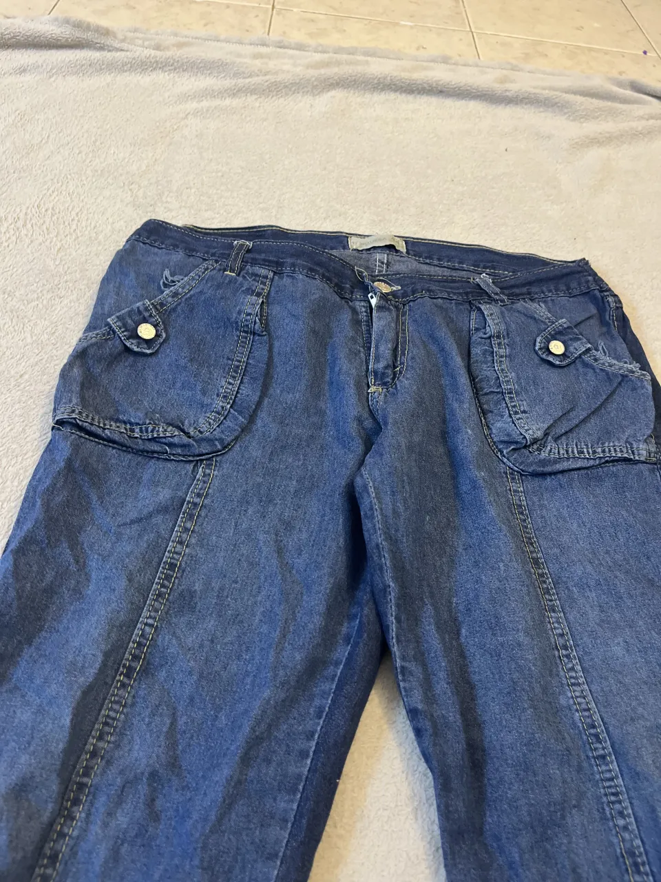 Pantalón pescador de jean azul con bolsillos cargo en los laterales y en la parte trasera. Posee detalles de costuras visibles y botones metálicos.