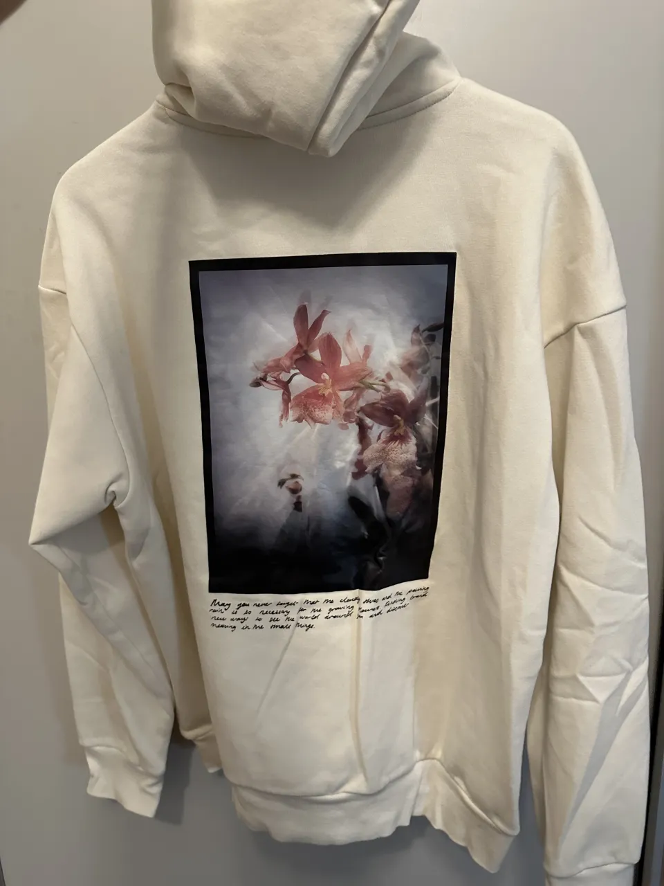 Hoodie de algodón color crudo con estampa de flores y texto en la espalda. Diseño oversize y súper cómodo, ideal para un look casual y relajado.