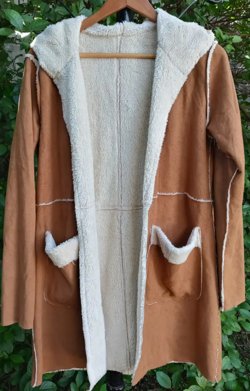 Tapado largo de mujer, con capucha y bolsillos. Interior de corderito beige, exterior marrón. Ideal para el invierno, abrigo y estilo en una sola prenda.