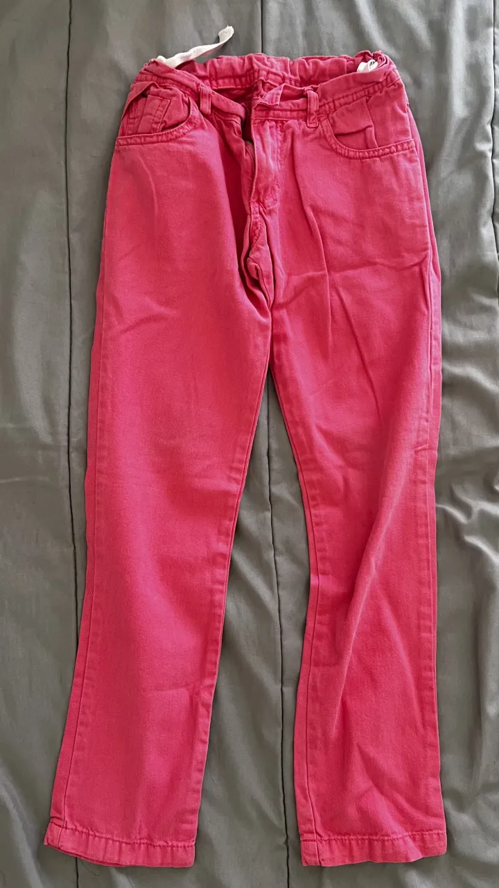 Pantalones de color rosa con cintura elástica y cordón ajustable. Presenta dos bolsillos delanteros y dos traseros. La prenda tiene un diseño simple y es adecuada para uso diario.