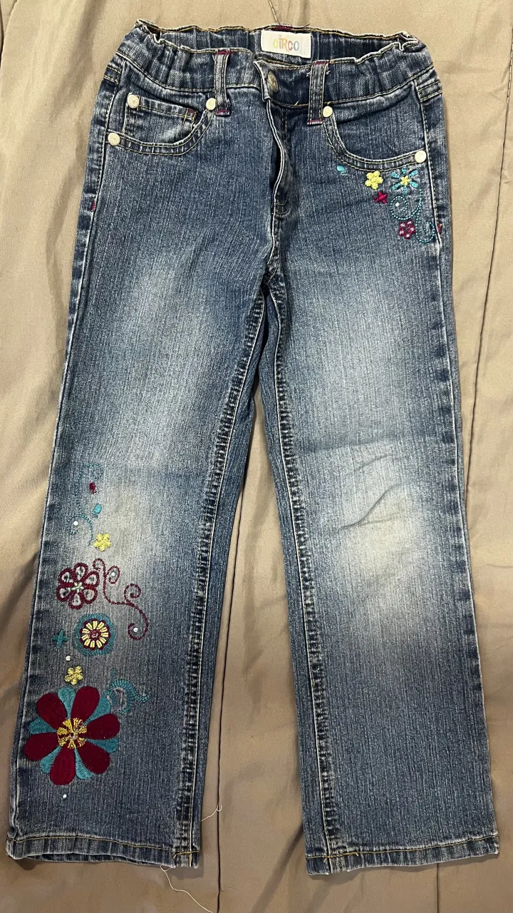 Jean de niña con bordados de flores en color fucsia, turquesa y amarillo en la parte delantera y trasera. Cintura elastizada.