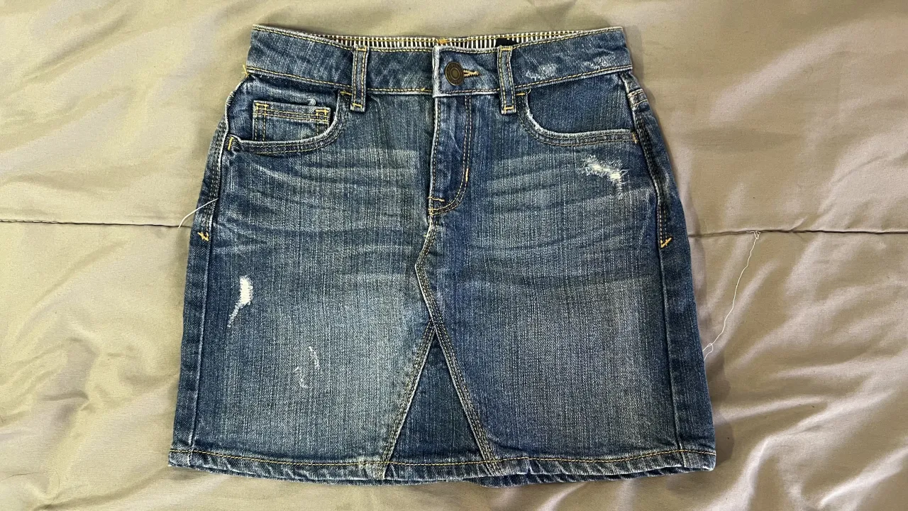 Pollera de jean azul con detalles de desgaste y roturas. Tiene bolsillos delanteros y traseros.