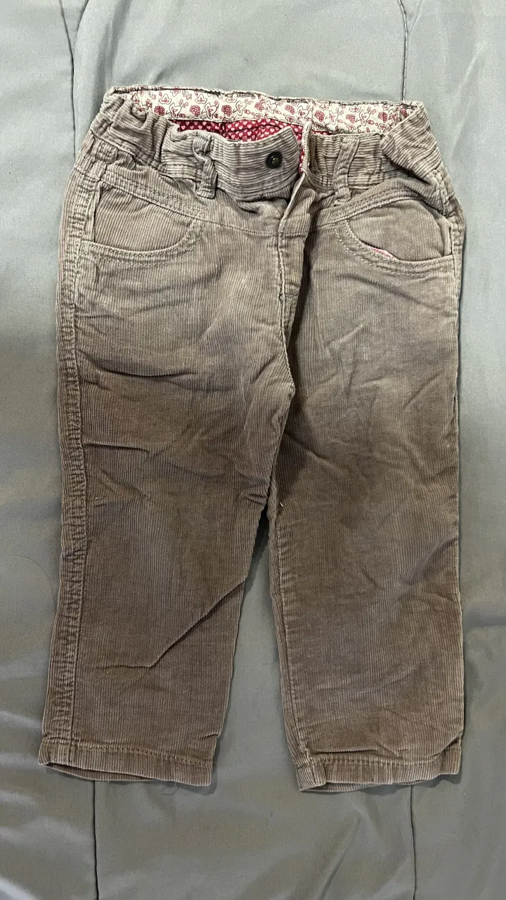 Pantalón de pana gris con cintura elástica y detalles de estampado floral en la cintura y bolsillos traseros con forma de moño.