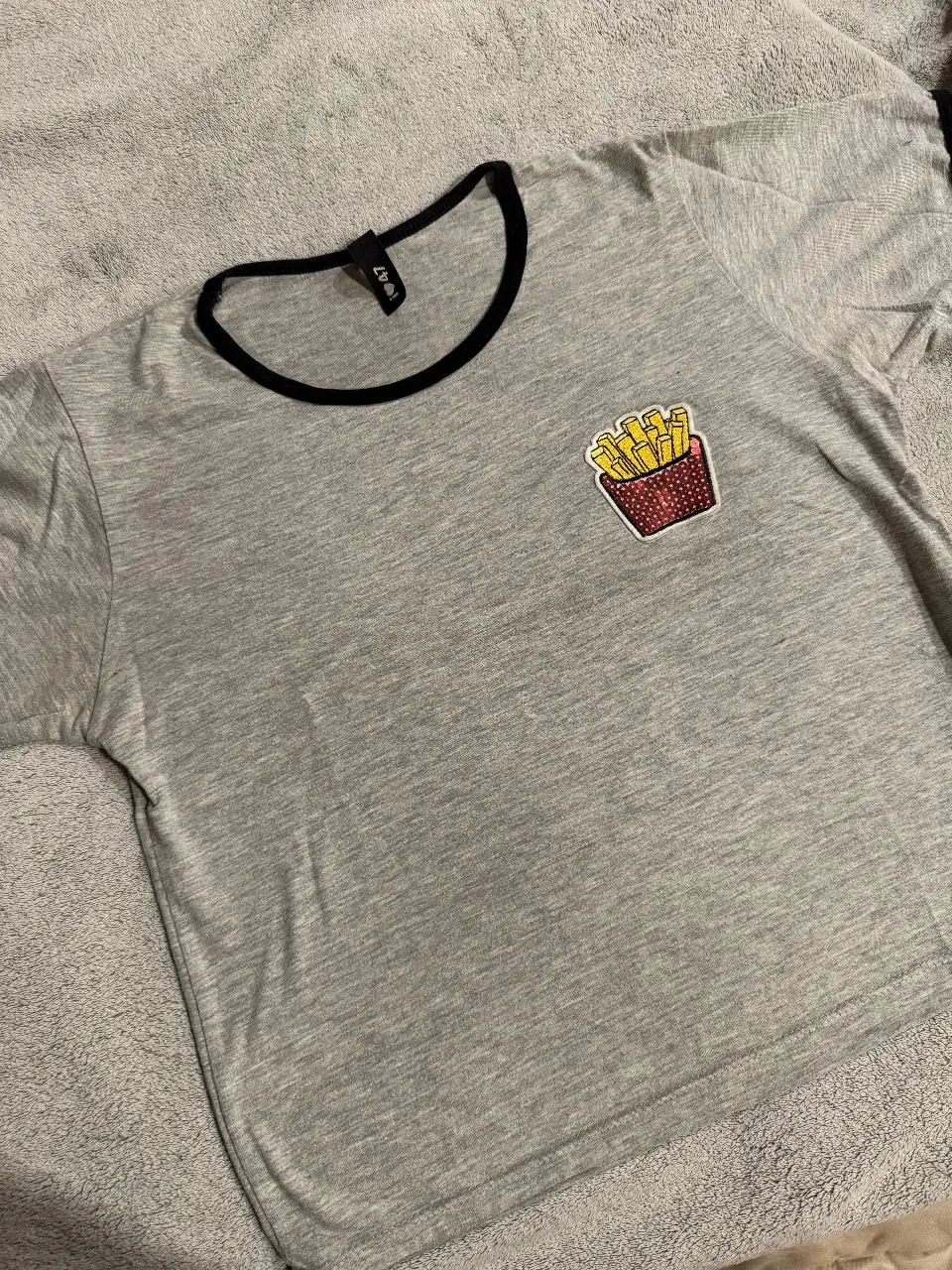 Remera gris de manga corta con cuello redondo negro y un parche de papas fritas en el pecho. Ideal para un look casual y divertido.