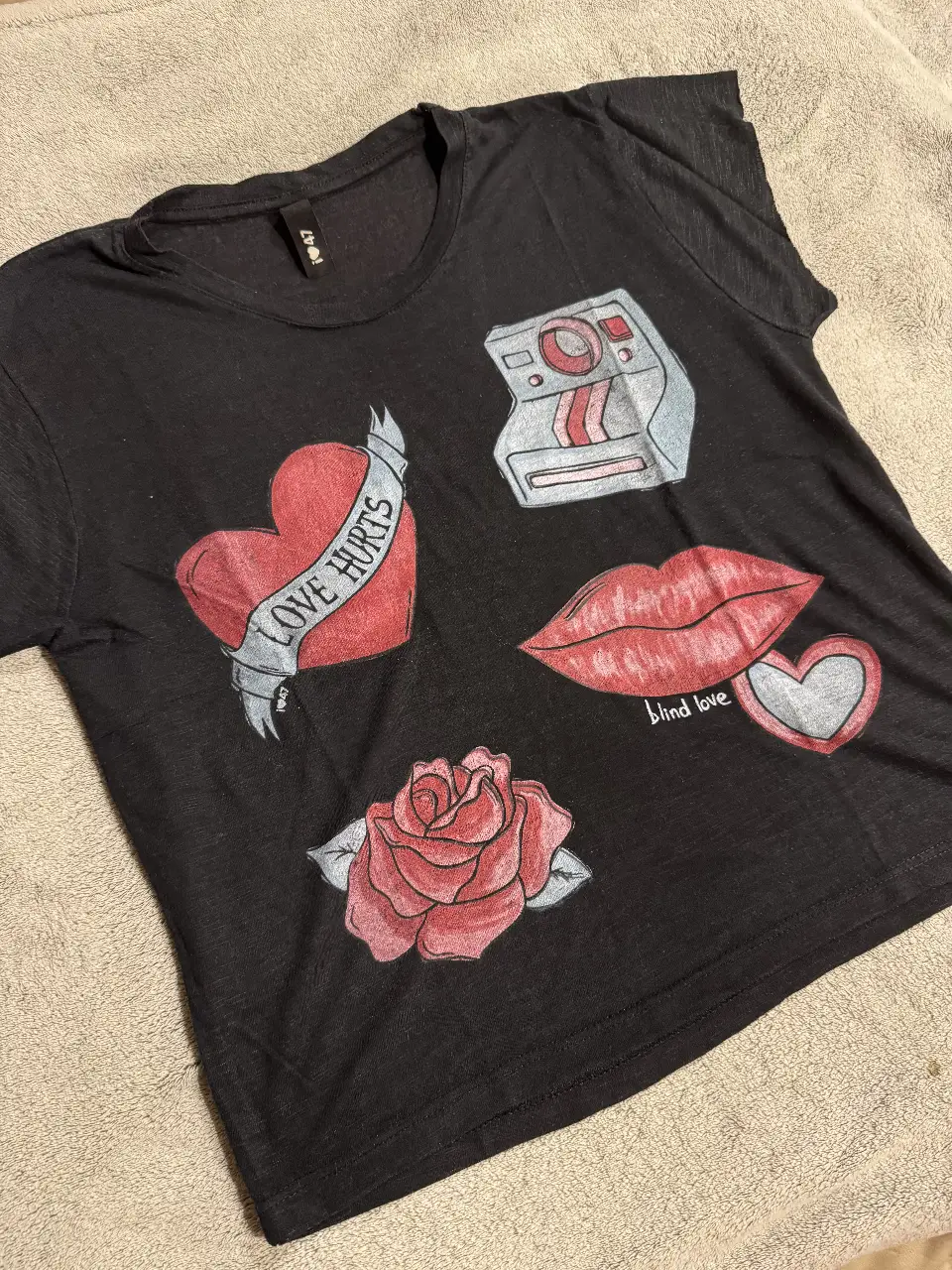 Remera negra con estampado de corazones, labios, rosa y cámara de fotos. Estilo vintage y romántico, ideal para un look casual y con onda.