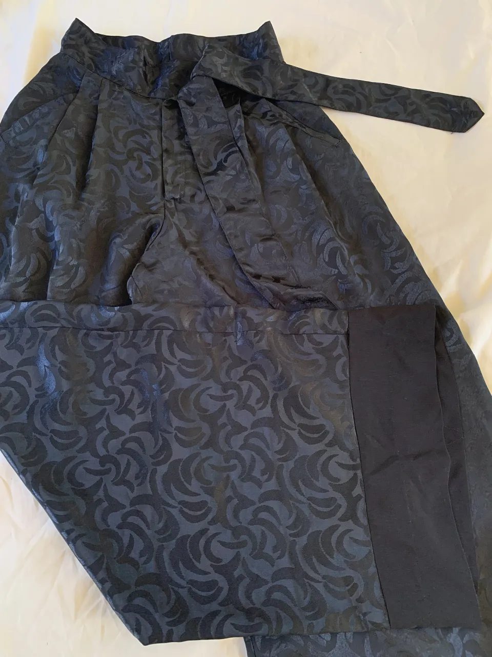 Pantalón palazzo de seda negro con estampado floral en relieve y lazo a la cintura. Un diseño elegante y sofisticado, perfecto para ocasiones especiales o para darle un toque chic a tu look.